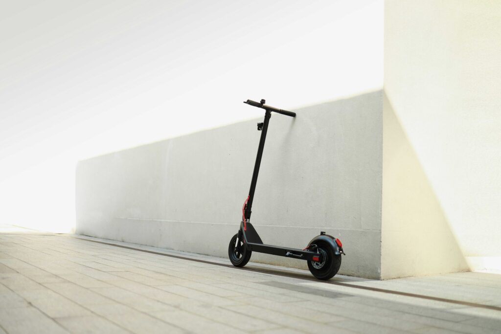 Patinete eléctrico negro apoyado contra una pared blanca en una acera